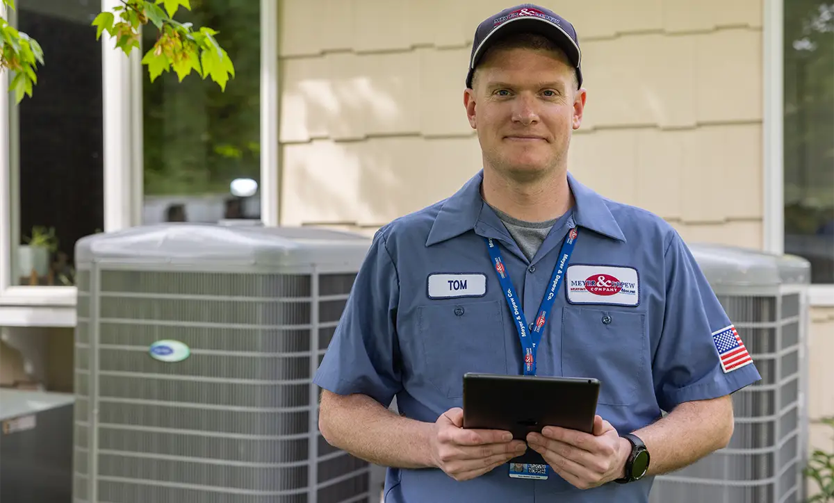 A technician standing in front of AC and heat pump units with a tablet.