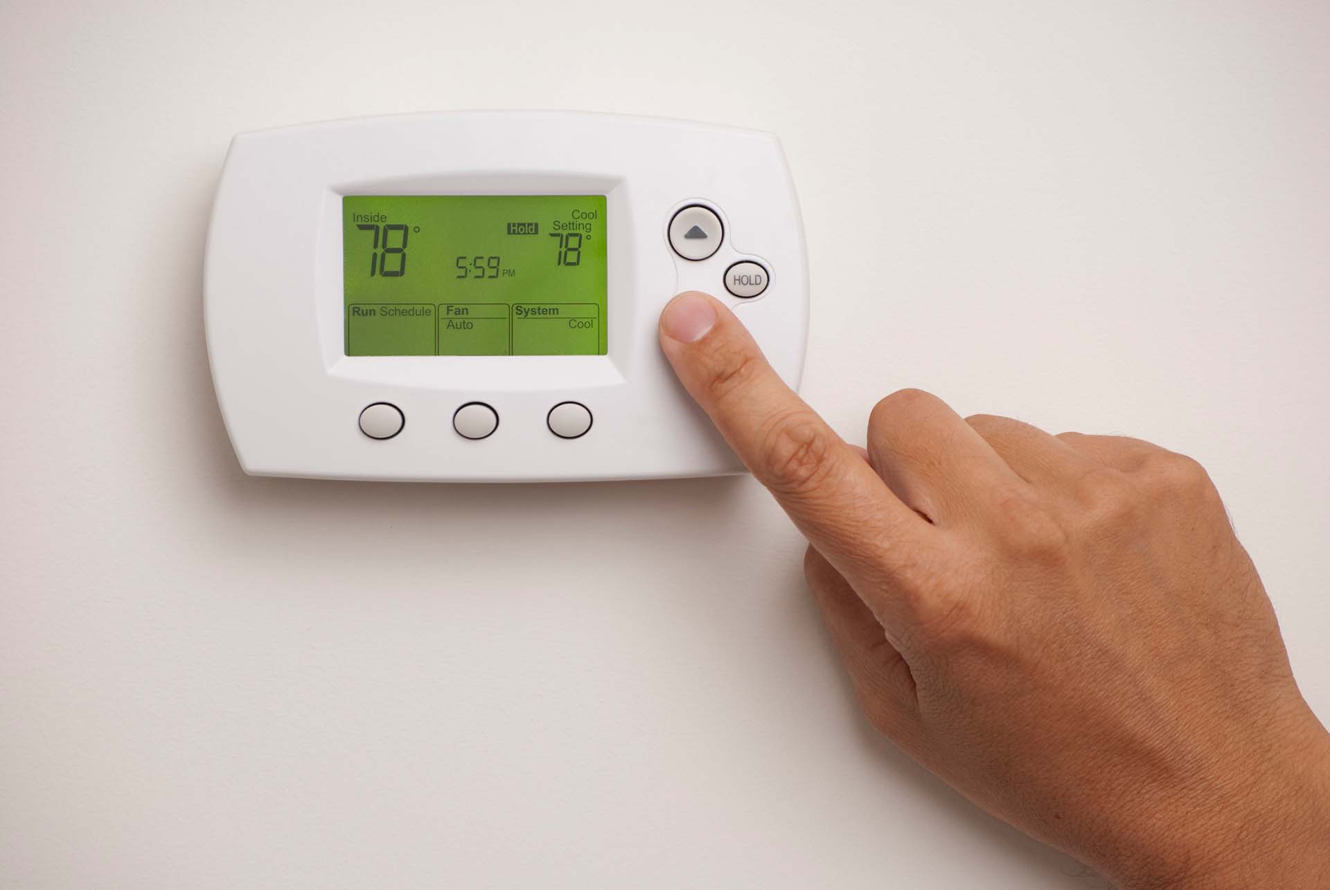 Hand pressing the down arrow on a thermostat to reduce the temperature
