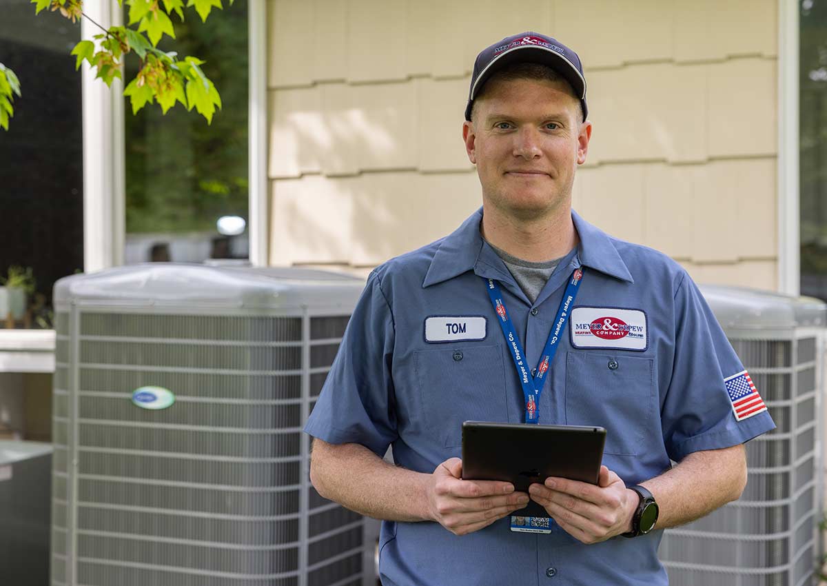 A technician standing in front of AC units with a tablet.